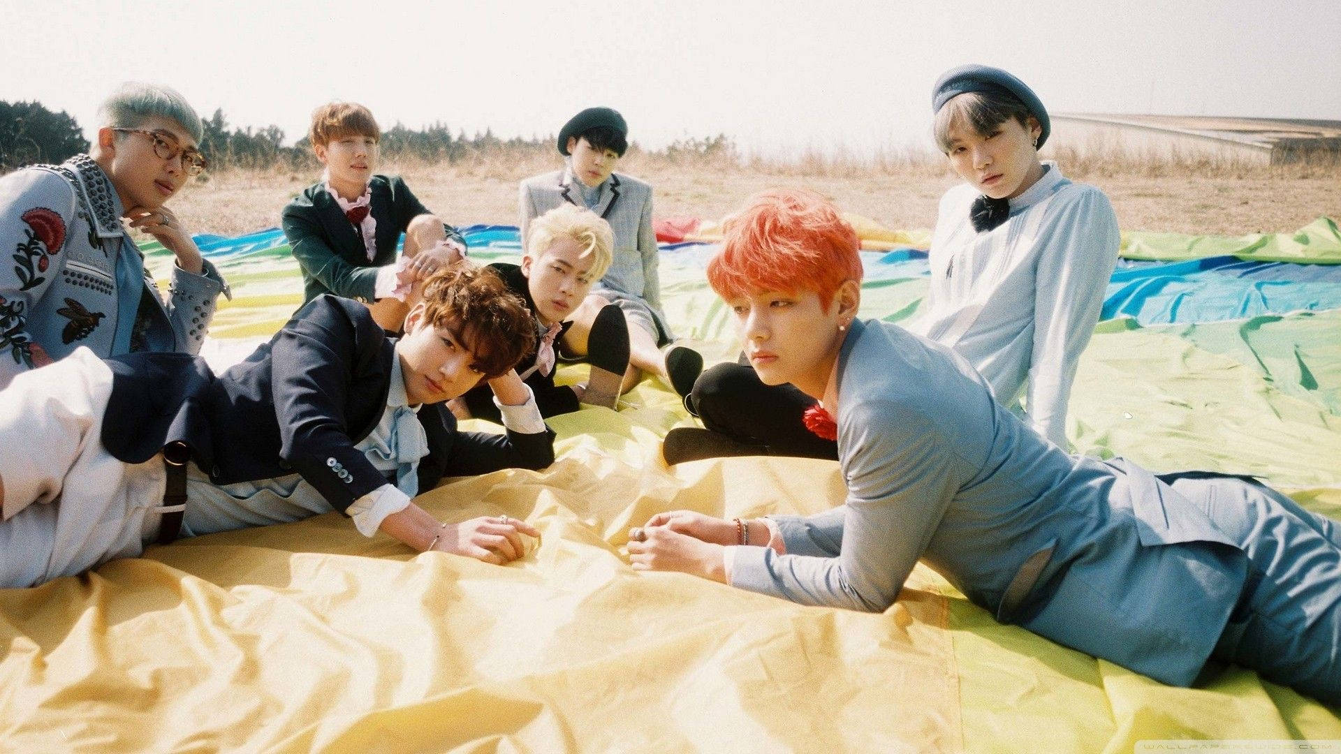 Участники BTS лежат на поле с ноутбуком Обои