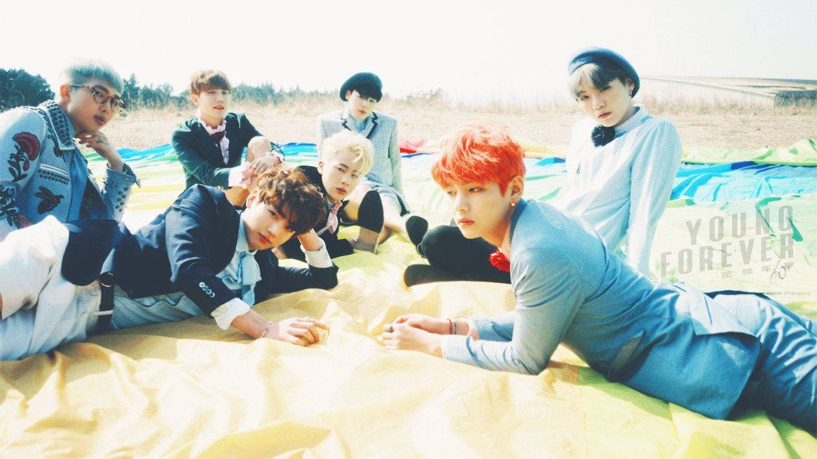 Участники BTS лежат на покрывале на пляже летом.
