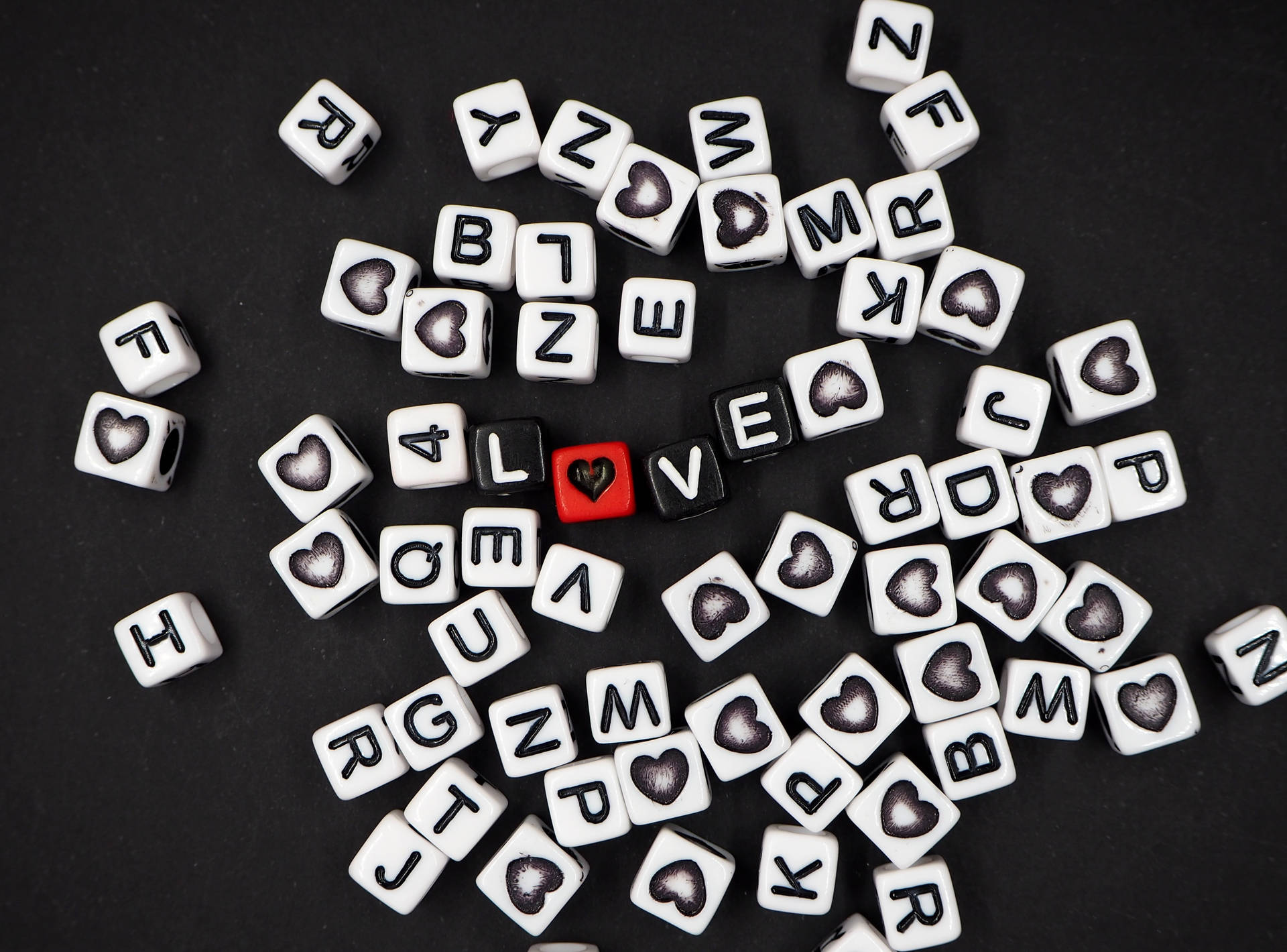 Черные игральные кости образуют слово «love» с сердцем вместо буквы «O» и разбросанные буквы белых костей на черной поверхности ко Дню сердца.