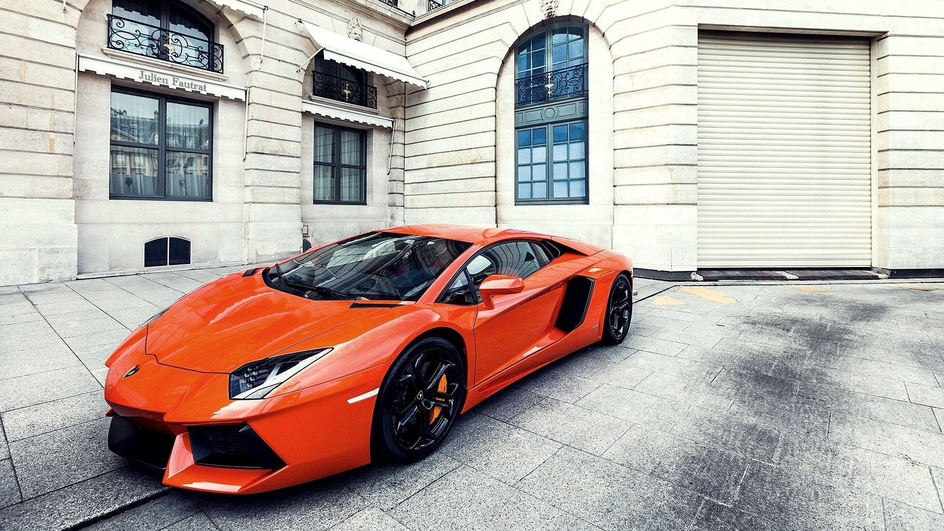 Обои с оранжевым Lamborghini Aventador на фоне здания.