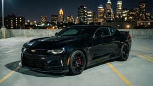 Обои Черный Camaro ZL1 стоит на крыше парковки на фоне ночного городского пейзажа.