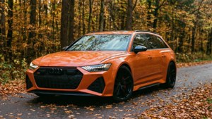 Оранжевый Audi RS6 Avant на осенней лесной дороге с падающими листьями.