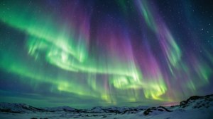 Яркое северное сияние с зелеными и фиолетовыми волнами над заснеженным пейзажем. — Вид на небо Обои